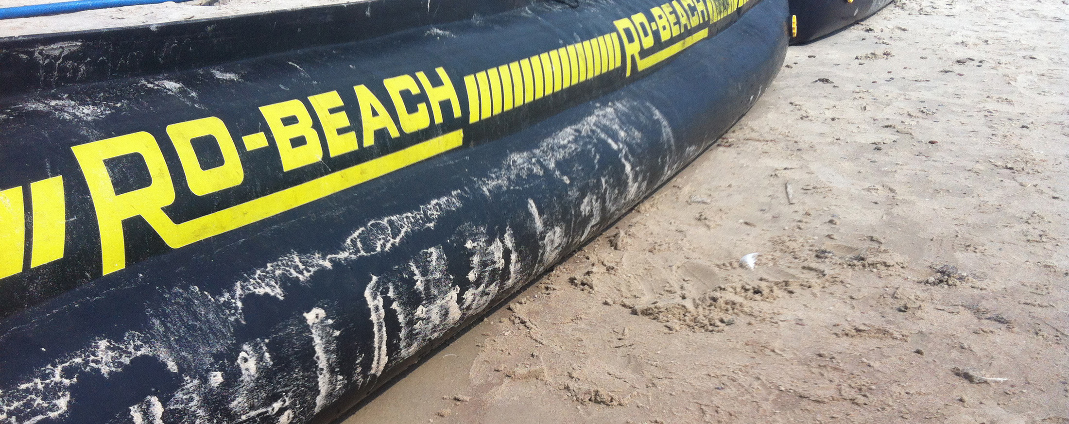 Inflatable black tube labeled "RO-BEACH" resting on sandy beach.