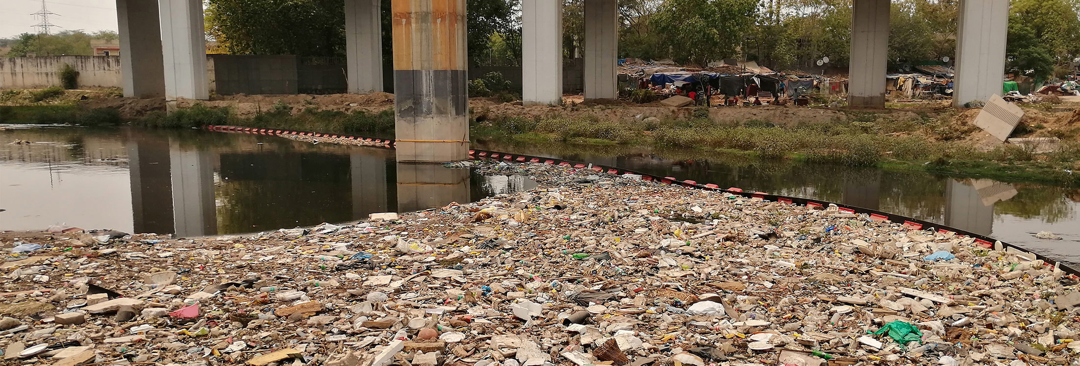 River filled with plastic waste under a bridge, highlighting pollution issues.