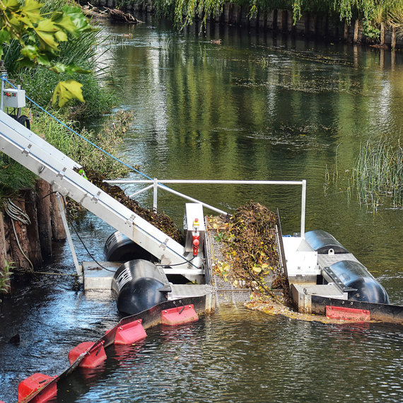Man operates a DESMI trash barrier system collecting debris in a river.