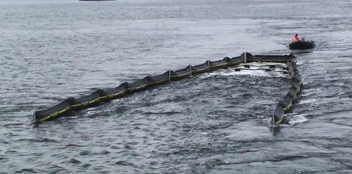 Oil containment boom deployed in water with a small boat nearby.